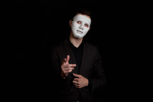 Portrait of a man in a white mask on a black background. He poin - Foto, Imagen
