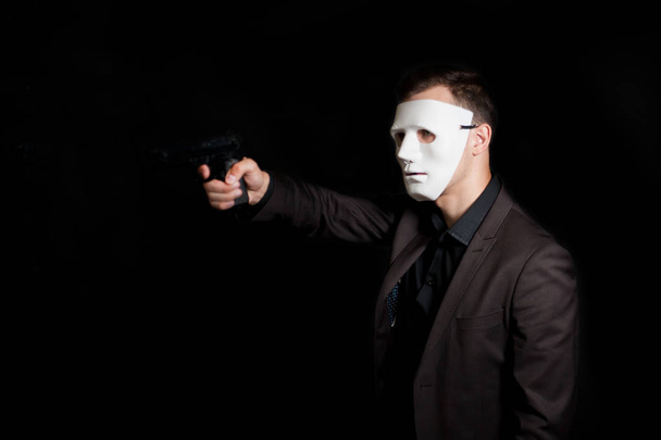 A man in a white mask on a black background, threatens with a gu - Foto, immagini