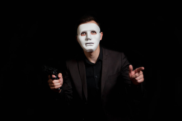 A man in a white mask on a black background, holding a gun. Robb - Fotó, kép