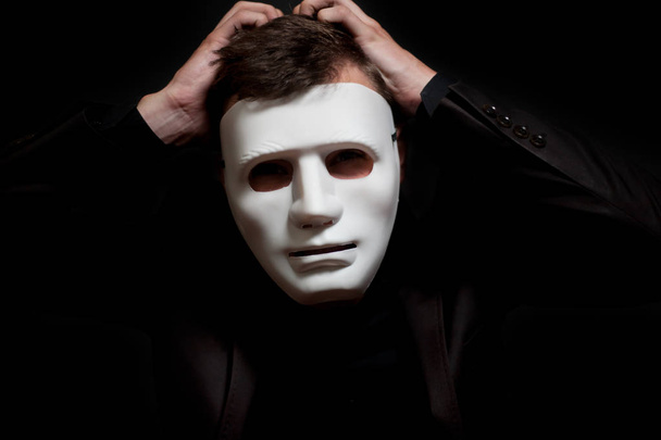 Közeli kép: egy férfi egy fehér maszkot, tartja a kezét a hajába - Fotó, kép