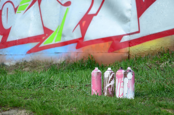 Несколько использованных банок с краской лежат на земле рядом со стеной с красивой картиной граффити. Уличное искусство и вандализм
. - Фото, изображение