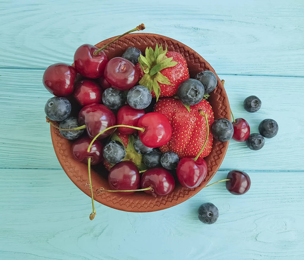 тарелка, ягоды, вишня, клубника, черника на голубом деревянном фоне
 - Фото, изображение