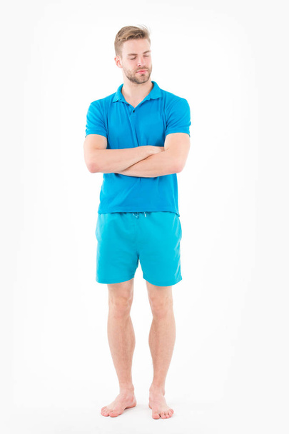 Man in tshirt and shorts barefoot isolated on white background. Bearded man with eyes closed in blue clothes. Macho in active wear for training. Sport fashion style and trend. Fitness and gym activity - 写真・画像