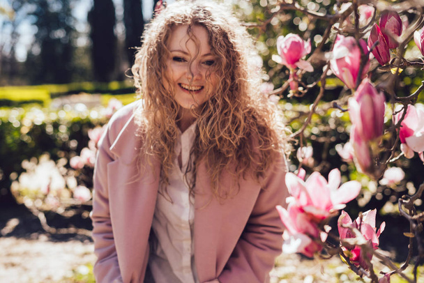 laughing curly young woman in pink coat enjoying the warmth and spring in the park - Foto, Bild