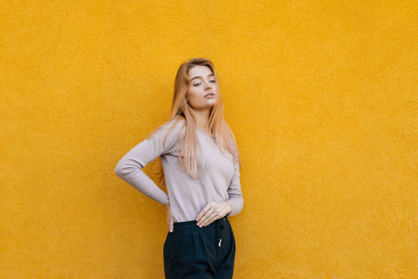 schattige jonge blonde model meisje poseren op gele muur achtergrond, stijlvolle kleding dragen - Foto, afbeelding