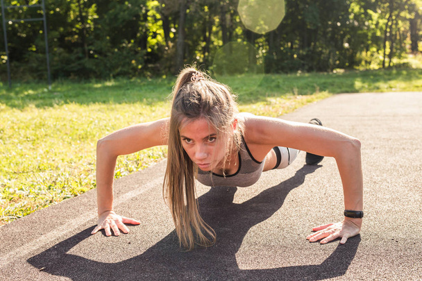 Fitness-nainen tekee punnerruksia ulkona harjoittelun aikana. Kaunis nuori ja hyväkuntoinen kunto urheilu malli koulutus ulkona puistossa
 - Valokuva, kuva