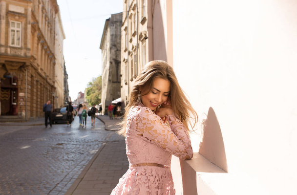 Εύθυμος μελαχρινή κοπέλα φορώντας ροζ δαντέλα φόρεμα, θέτοντας στο δρόμο κατά τη διάρκεια μια ηλιόλουστη ημέρα - Φωτογραφία, εικόνα