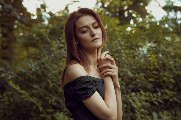 Krásná mladá žena nosí černé šaty s nahá ramena, pózuje v lese - Fotografie, Obrázek