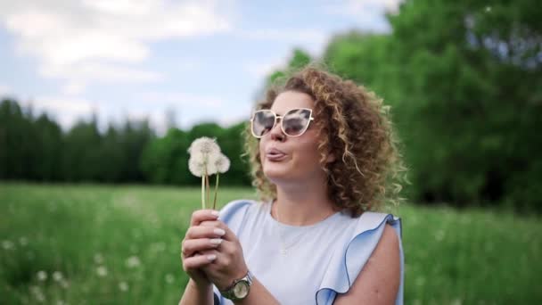 Güneş gözlükleri çekici kadın karahindiba darbeler ve rüzgarla uçup, güzel kinky kız dandelions yaz güneşli bir günde yeşil Park'ta dinlenme Rüzgar uçurdu - Video, Çekim