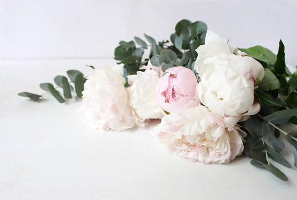 Styled stock photo. Decorative still life floral composition. Wedding or birthday bouquet of pink and white peony flowers and eucalyptus branches. White table background. - Foto, imagen