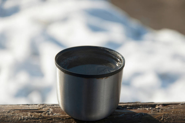 Крышка вакуумной фляжки с горячим чаем на открытом воздухе в солнечный и морозный зимний день
 - Фото, изображение