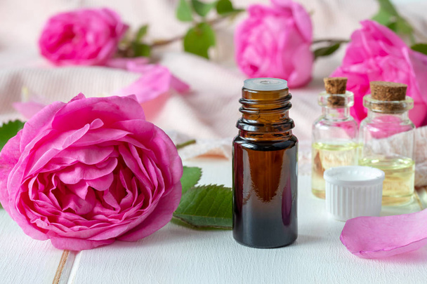 Uma garrafa escura de óleo essencial com rosas em uma mesa branca
 - Foto, Imagem