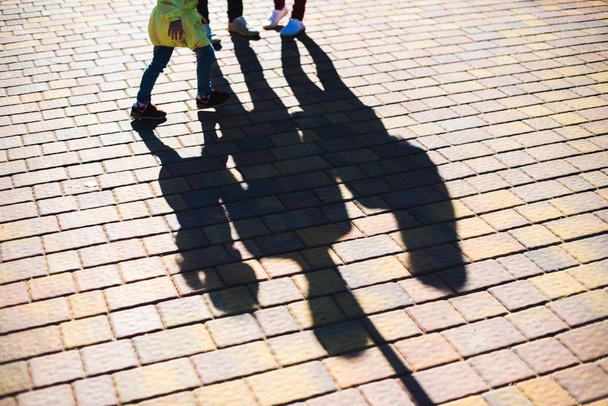 Long shadows of people on the sidewalk tiles in the urban environment at the dawn or dusk - Photo, image