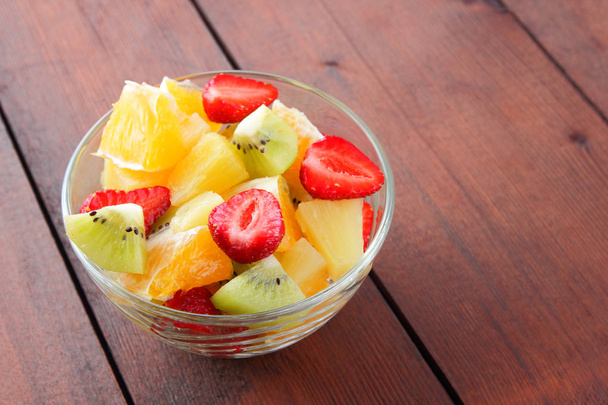 Insalata di frutta da ananas, kiwi, arancia, fragola. Frutta a fette multicolore in un piatto trasparente. Cibo vegetariano su uno sfondo di legno. Agrumi per la cucina asiatica
 - Foto, immagini