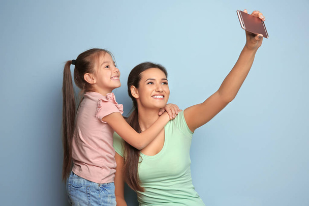 Young mother with little daughter taking selfie on color background - Foto, imagen