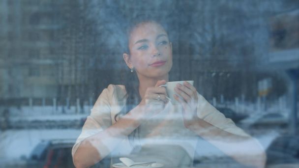 Dreamy young woman with a cup of tea at a cafe watching city life - 写真・画像