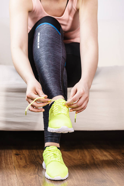 Woman in sportswear sitting on sofa indoor getting ready for exercises. Tying up shoes - Photo, Image