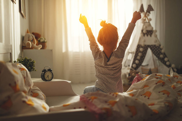 child girl wakes up in morning in bed and stretches by windo - Фото, зображення