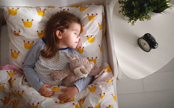  child  girl sleeps in her bed with a toy teddy bear  in mornin - Fotografie, Obrázek