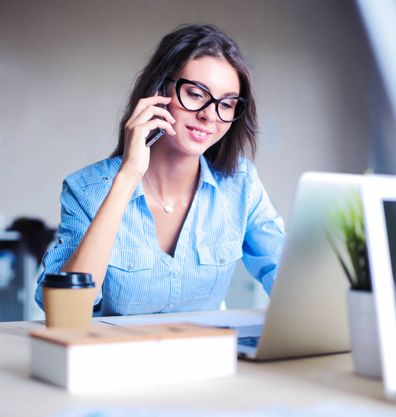 Beautiful young business woman sitting at office desk and talking on cell phone. Business woman - Foto, Bild
