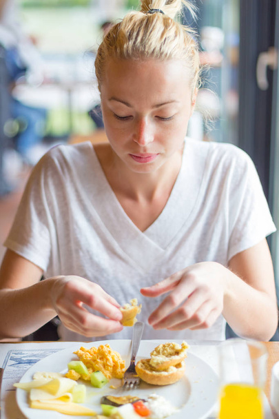 mulher comendo delicioso café da manhã saudável: ovos mexidos, queijo, legumes, pão e suco de laranja
. - Foto, Imagem