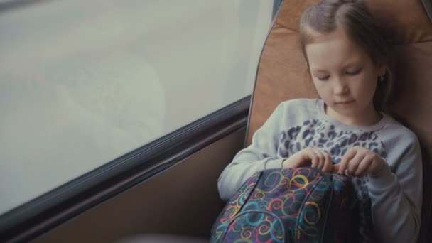 Joven, hermosa pasajera con bolso escolar en el autobús escolar en movimiento utilizando la red social en su teléfono inteligente y mirando por la ventana
. - Imágenes, Vídeo