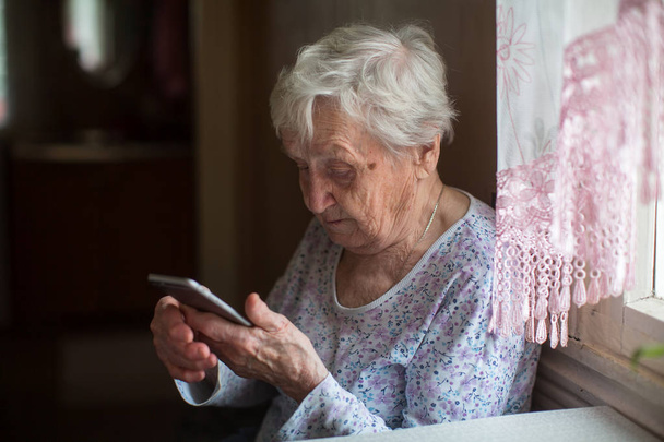 Oudere vrouw met een smartphone in huis. - Foto, afbeelding