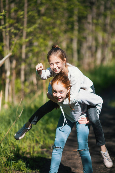 Дві сестри дівчата друзі підлітки катаються один на одного розважаючись в парку влітку
 - Фото, зображення
