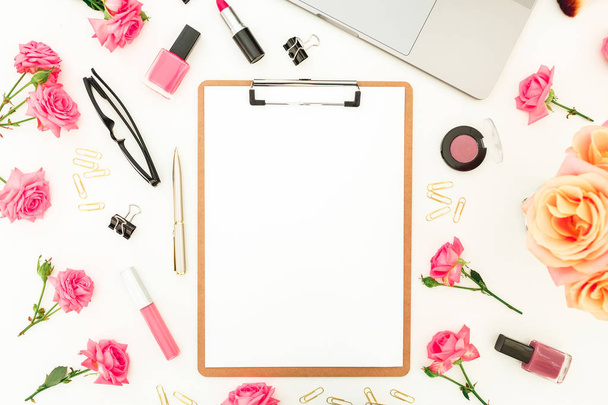 Draufsicht auf rosa Rosenblüten, Laptop, Make-up-Set und Klemmbrett isoliert auf weißem Hintergrund - Foto, Bild