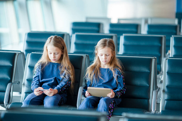 Pequenas garotas adoráveis no aeroporto à espera de embarque brincando com laptop
 - Foto, Imagem