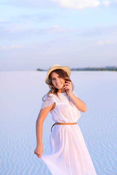Young jocund girl walking bareffot on sand, weaaring white dress - Photo, image