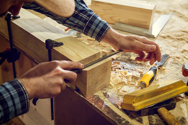 Detailní záběr zkušený tesař v pracovní oděvy a malé buiness majitel pracuje v dílně dřeva, pomocí dláta vyřezávání ze dřeva v dílně na stole je kladivo a mnoho nástrojů  - Fotografie, Obrázek