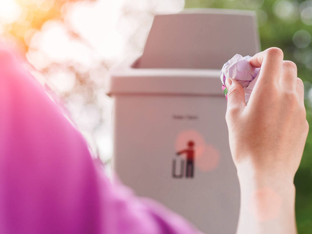 Eine weibliche Hand wirft ein Papier in einen Mülleimer auf Bokeh-Hintergrund. Reinigungskonzept. - Foto, Bild