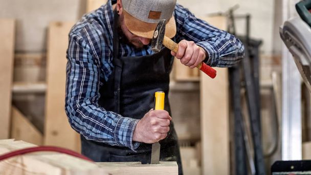 Fuerte carpintero en ropa de trabajo tallando madera usando una herramienta de carpintería, cincel, manos cerca, carpintería y concepto de artesanía
 - Foto, Imagen