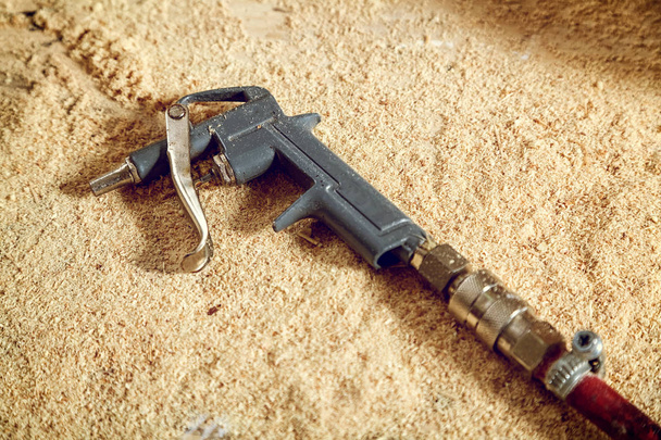 Gros plan d'un vieux pistolet métallique pour souffler l'air pour nettoyer la sciure de bois dans l'atelier
 - Photo, image