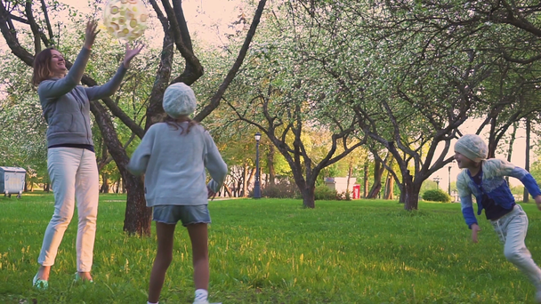sport s míčem na jaře parku v kvetoucí zahradě hrají rodiče a dvě dcery. Aktivní odpočinek. - Záběry, video
