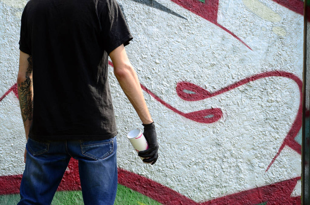 Молодий хуліган з розпилювачем може стояти на бетонній стіні з графітовими картинами. Нелегальна концепція вандалізму. Вуличне мистецтво
. - Фото, зображення