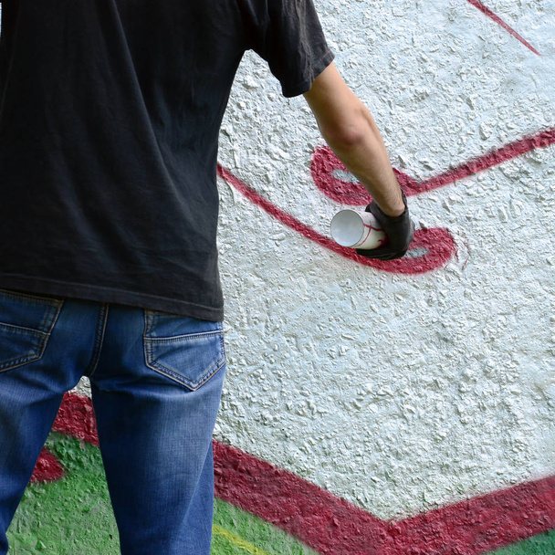 Um jovem hooligan pinta grafite em uma parede de concreto. Conceito de vandalismo ilegal. Arte de rua
. - Foto, Imagem