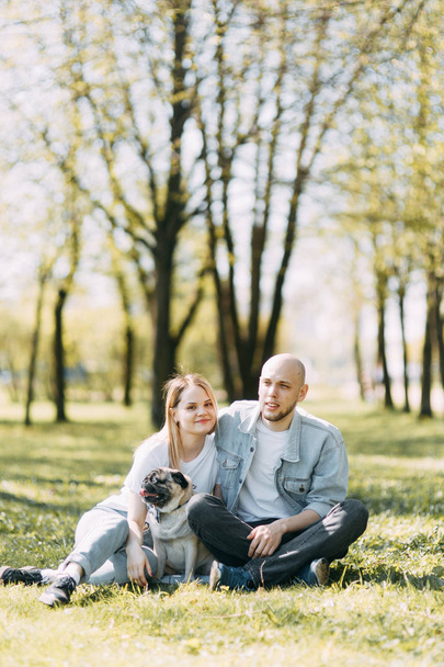 Beautiful young couple in the Park on a Sunny day, loving and happy. Walk and laugh with the dog. Pre-wedding shooting in nature. Casual style in clothing and European in processing - Foto, Imagen
