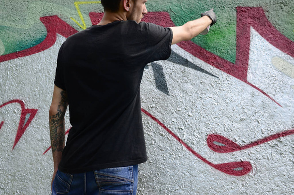 Nuori huligaani maalaa graffitin betoniseinään. Laiton ilkivalta. katutaide
. - Valokuva, kuva