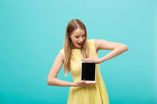 Opgewonden geschokt knappe jonge vrouw in gele jurk hebben verward of verbaasd uitdrukking op gezicht terwijl u ontvangt dringend bericht of e-mail, met behulp van wi-fi op Tablet PC. - Foto, afbeelding