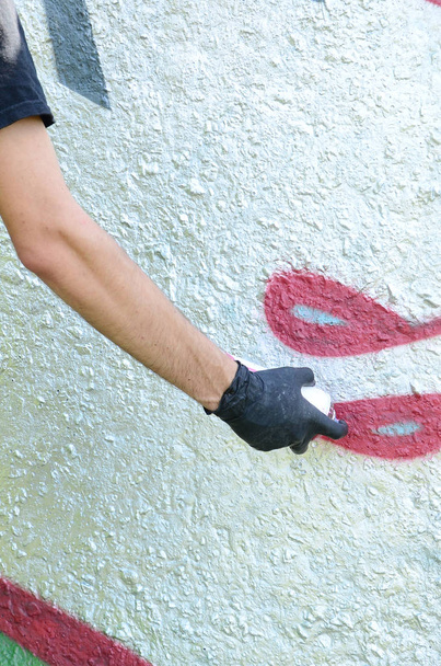 Eine Hand in schwarzen Handschuhen malt Graffiti auf eine Betonwand. Illegaler Vandalismus. Straßenkunst. - Foto, Bild