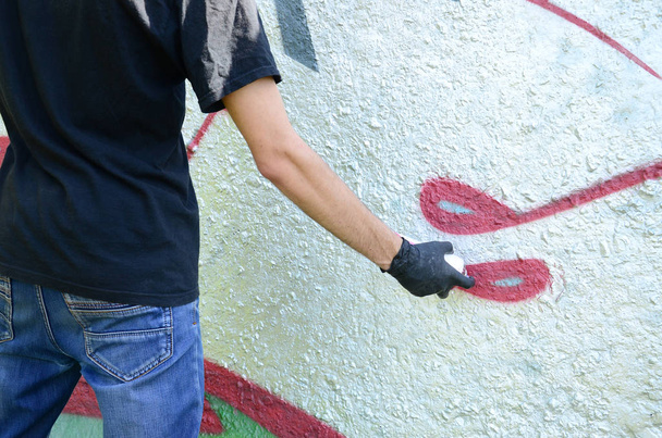 A young hooligan paints graffiti on a concrete wall. Illegal vandalism concept. Street art. - Φωτογραφία, εικόνα