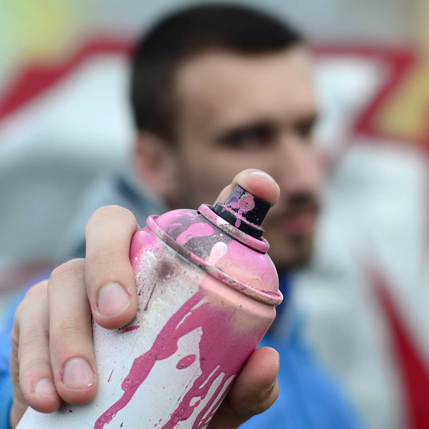Un giovane graffitista in giacca blu tiene davanti a sé una lattina di vernice su uno sfondo di graffiti colorati. Street art e concetto di vandalismo
. - Foto, immagini