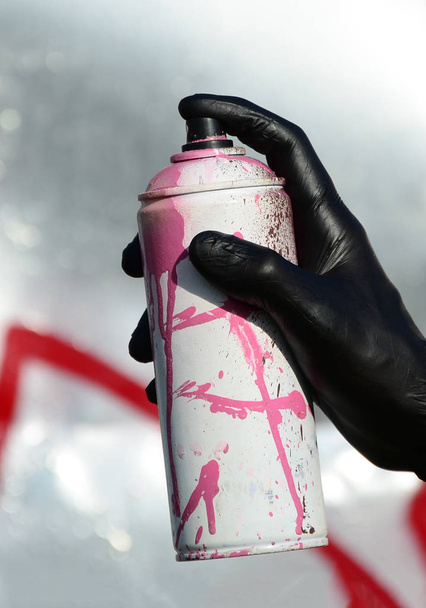 Una mano con una lata de spray que dibuja un nuevo graffiti en la pared. Foto del proceso de dibujar un graffiti en una pared metálica. El concepto de arte callejero y vandalismo ilegal
. - Foto, Imagen