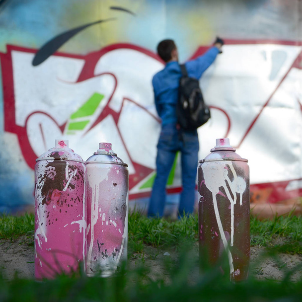 Ein paar gebrauchte Farbdosen vor dem Hintergrund des Raumes mit der Wand, auf die der junge Mann eine große Graffiti-Zeichnung zeichnet. Moderne Kunst, Wände in Graffiti zu zeichnen. - Foto, Bild
