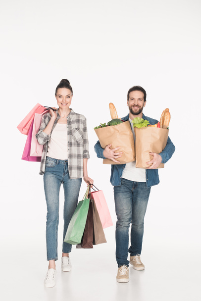 cheerful wife and husband carrying shopping bags and paper packages full of food isolated on white - Fotografie, Obrázek