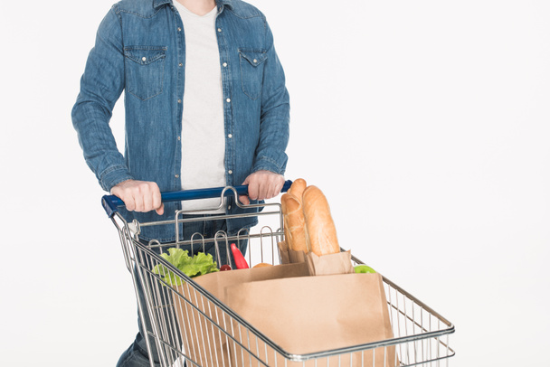 částečný pohled člověka s nákupním vozíkem plným papírových obalů s jídlem izolované na bílém - Fotografie, Obrázek