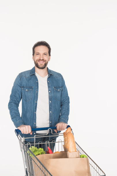 portrait of smiling man with shopping cart full of paper packages with food isolated on white - Valokuva, kuva