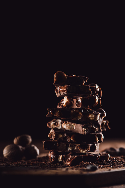 closeup shot of stack of chocolate pieces and nutmegs on black background  - Valokuva, kuva